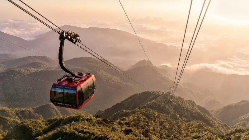 Red cable car gliding over green mountains and clouds at Ba Na Hills