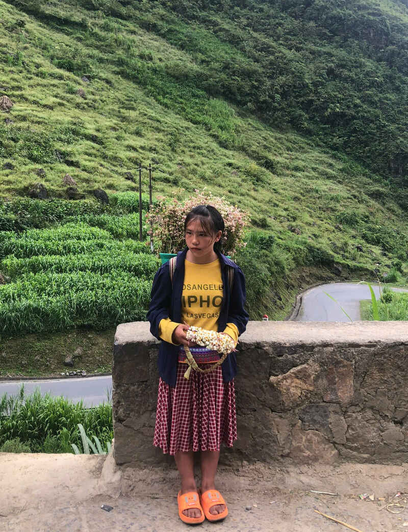 Hmong girl in traditional skirt selling handmade flowers on Tham Ma Pass in Ha Giang Loop Vietnam